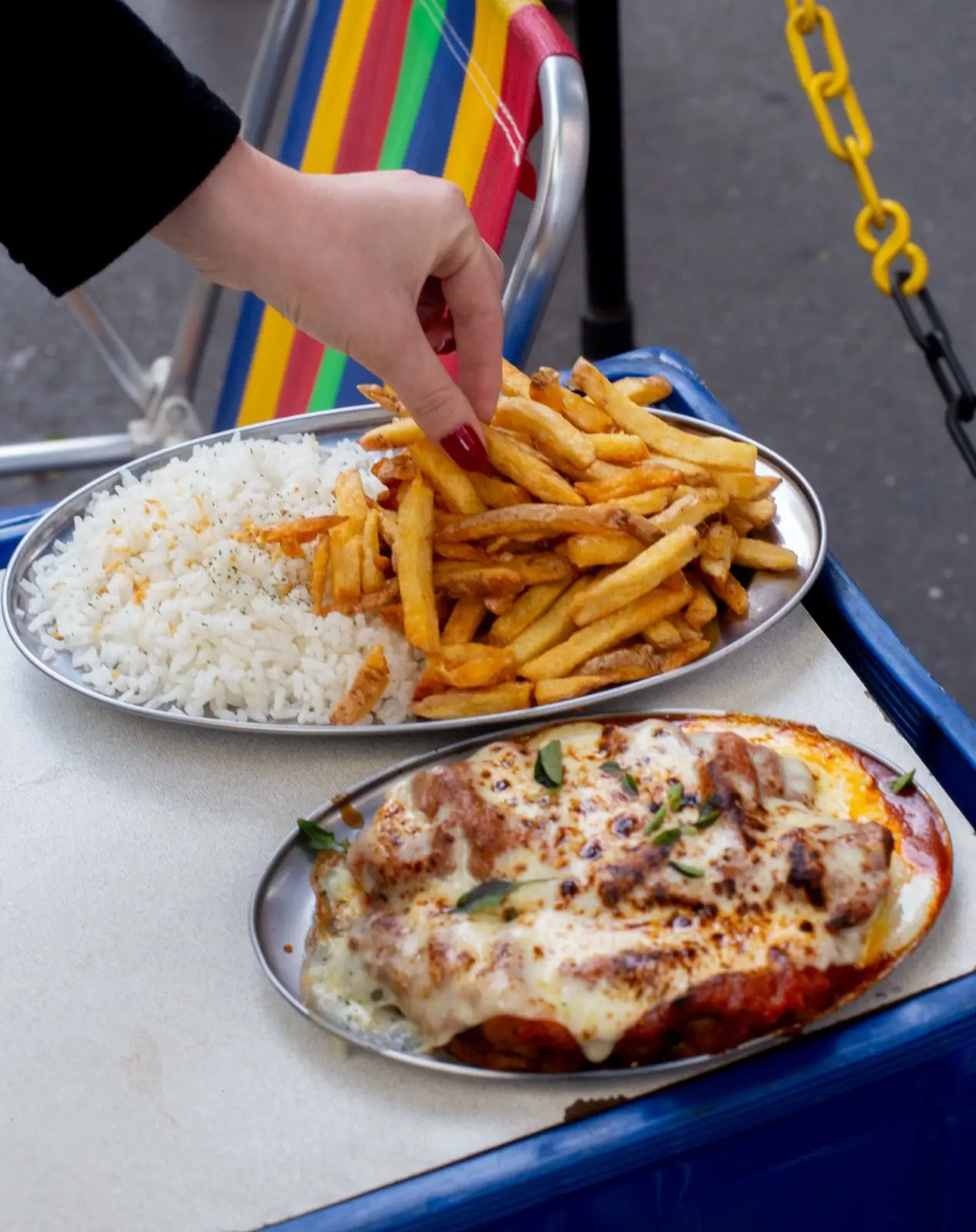 Travessas de arroz, batatas fritas e milanesa gratinada numa mesa na calçada